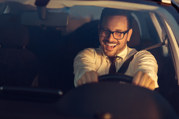 Happy businessman driving a car at sunset
