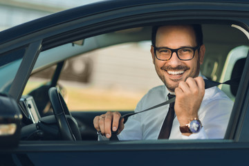 Happy businessman fastening his seat belt in a car