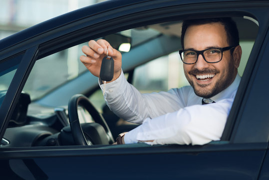 Happy man sitting in a car and holding new car keys