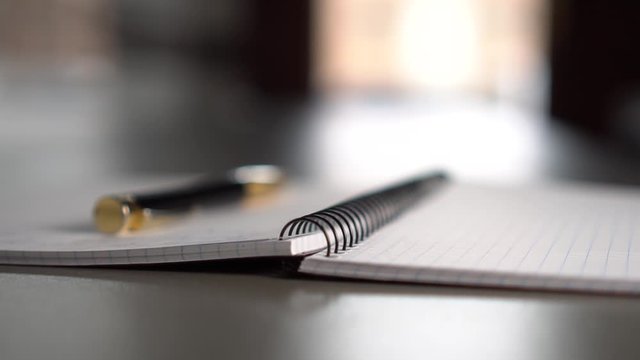 A black-gold pen lies on an open notebook on a gray table in front of a window. The concept of life planning and working day in business