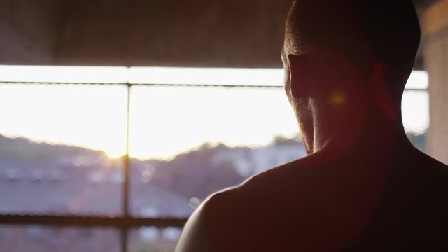 Topless male with fitness monitor on his wrist strokes his head looking out to the sunlight, in slow motion 