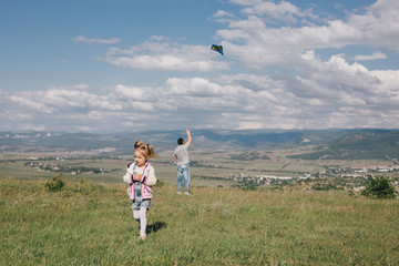 Happy family flying a colorful kite on green meadow.