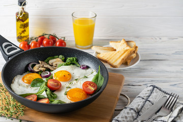 Healthy breakfast with fried eggs, tomatoes, mushrooms and spinach leaves served in frying pan