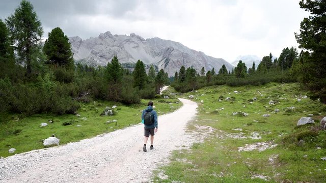 Man hiking in alta via N1 in Dolomite Alps mountains in a sunny summer cloudy day surrounded with green grass and forest
