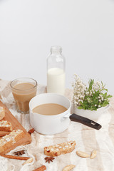 Coffee with milk, cookies, cinnamon and fruits on the tablecloth.