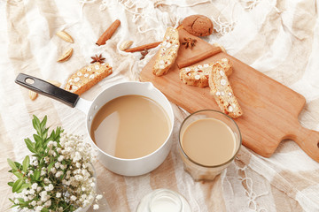 Coffee with milk, cookies, cinnamon and fruits on the tablecloth.