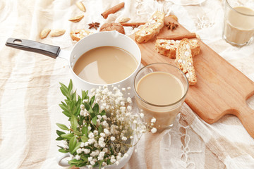 Coffee with milk, cookies, cinnamon and fruits on the tablecloth.