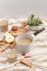 Coffee with milk, cookies, cinnamon and fruits on the tablecloth.