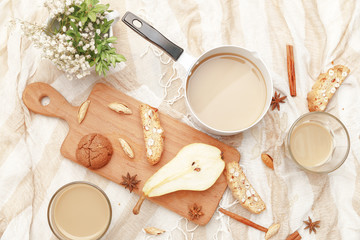 Coffee with milk, cookies, cinnamon and fruits on the tablecloth.