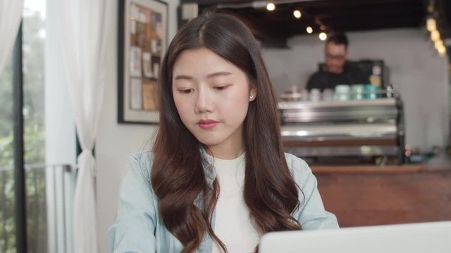 Young Asian freelance women working on laptop at coffee shop. Asian happy girl barista waiter wear gray apon serve hot cup of coffee to female customer who business work in cafe or restaurant.