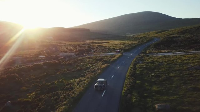 Aerial view of a road in Wicklow Mountains, drone flying backwards and a sun flare.