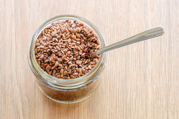 Whole flax seeds in a glass jar with metal spoon on a wooden table. Healthy food for lower cholesterol and preventing heart diseases.