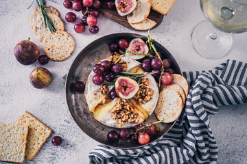 Fancy baked brie cheese platter with honey and walnuts, fresh rosemary. Red grapes, figs and white wine