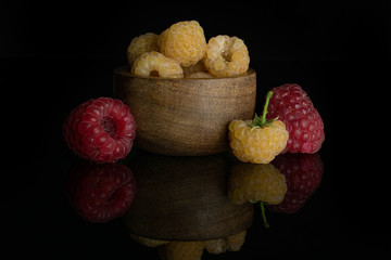 Lot of whole fresh golden hymalayan raspberry with two red berries in wooden bowl isolated on black glass