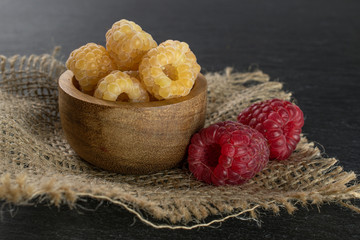 Lot of whole fresh golden hymalayan raspberry with two red berries in wooden bowl on jute cloth on...