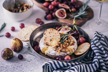 Fancy baked brie cheese platter with honey and walnuts, fresh rosemary. Red grapes, figs and white wine