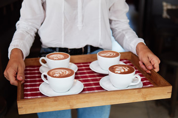 Female barista hands holding tray with set of cups fresh delicious cappuccino with latte art cream foam, brewed and made with love and take care concept, good service coffee shop