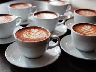 Set of freshly brewed cappuccino cups with milk foam latte art served on bartend table in cozy city cafe lit with natural window light