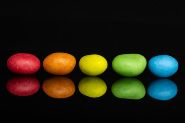 Group of five whole sugared nut dragee rainbow isolated on black glass