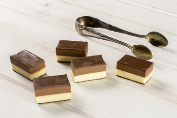 Group of five whole mellow two coloured nougat piece with sugar tongs on white wood