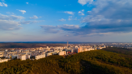 Shot of a beautiful city located at the edge of a forest, and a cloudy sky, during sunrise.