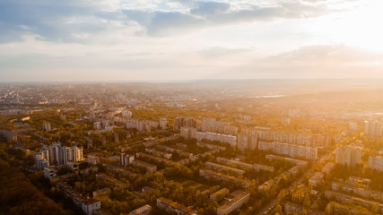 Shot of a city located at the edge of a forest, and a cloudy sky, during sunrise.