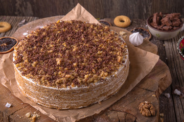 Delicious honey cake with sweet sour cream, chocolate and nuts on a rustic background. View from above. Free space for text.