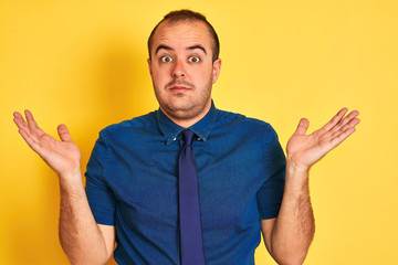 Young businessman wearing denim casual shirt and tie over isolated yellow background clueless and...