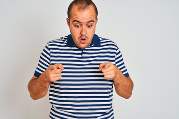 Fototapeta premium Young man wearing casual striped polo standing over isolated white background Pointing down with fingers showing advertisement, surprised face and open mouth