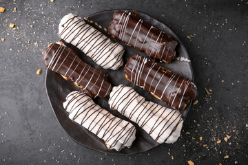 Eclairs or profiteroles with chocolate and custard cream on a metal plate on a dark background. Traditional French dessert. Empty space for design text template. Top view.