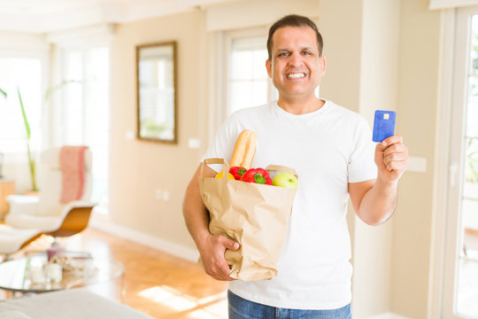 Middle age man holding groceries bag and showing credit card