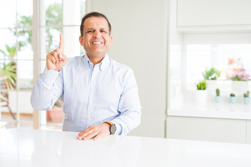 Middle age man sitting at home showing and pointing up with finger number one while smiling confident and happy.