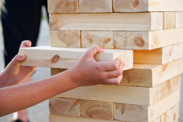A child takes out one bar from the tower while playing a giant jenga. Outside