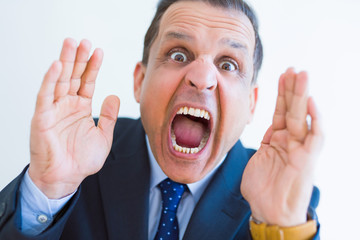 Middle age man shouting crazy with hands over mouth over white wall background