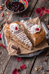 Sliced honey cake with caramel and whipped cream. A piece of dessert on wooden boards.