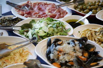 An assortment of healthy food on the buffet table - Prosciutto, seafood, salad, olives and pasta