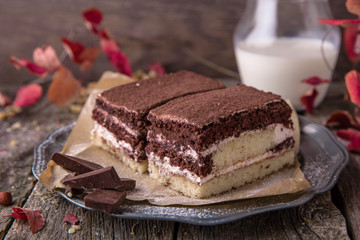 Sliced Tiramisu cake made of chocolate and white sponge. A piece of dessert on wooden boards.