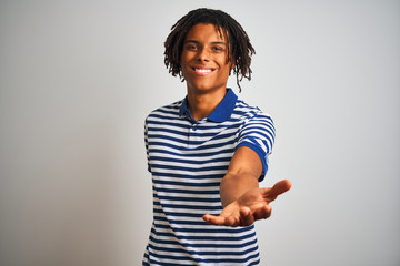 Obraz premium Afro man with dreadlocks wearing striped blue polo standing over isolated white background smiling cheerful offering palm hand giving assistance and acceptance.
