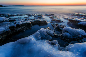 Beautiful seascape. Large rocks covered with ice are flooded with sea water during dawn.