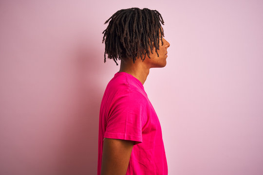 Afro american man with dreadlocks wearing t-shirt standing over isolated pink background looking to side, relax profile pose with natural face with confident smile.