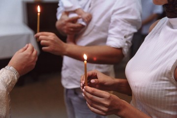 Obraz na płótnie Canvas view of women and a man, holding in hands candles and a baby during the Epiphany in russian orthodox church
