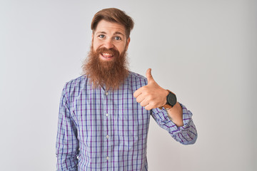 Young redhead irish man wearing casual shirt standing over isolated white background doing happy thumbs up gesture with hand. Approving expression looking at the camera with showing success.