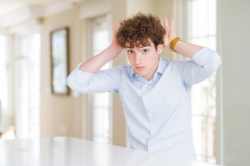 Young business man with curly read head Doing bunny ears gesture with hands palms looking cynical...