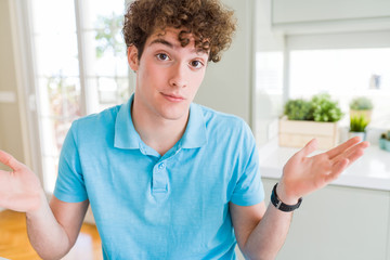 Young handsome man wearing casual blue t-shirt at home clueless and confused expression with arms...