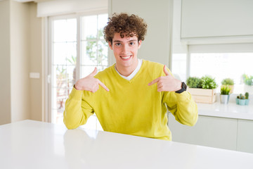 Young handsome man wearing yellow sweater at home looking confident with smile on face, pointing...