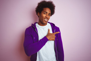 Young african american man wearing purple sweatshirt standing over isolated pink background cheerful with a smile on face pointing with hand and finger up to the side with happy and natural expression