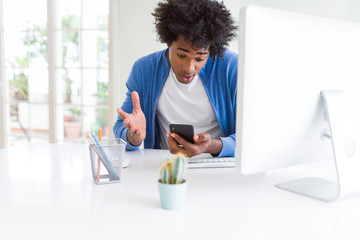 African American man working using smartphone and computer scared in shock with a surprise face, afraid and excited with fear expression