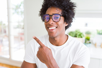 African American man wearing glasses cheerful with a smile of face pointing with hand and finger up to the side with happy and natural expression on face