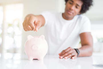 Close up of african american man saving money putting a coin inside piggy bank