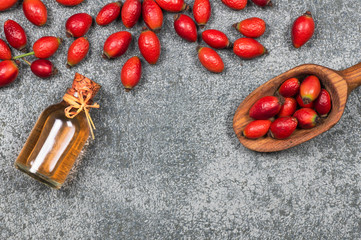 Glass bottle of rosehip seed essential oil with fresh rose hip fruits on grey rustic background. Dogrose oil with fresh dog roses